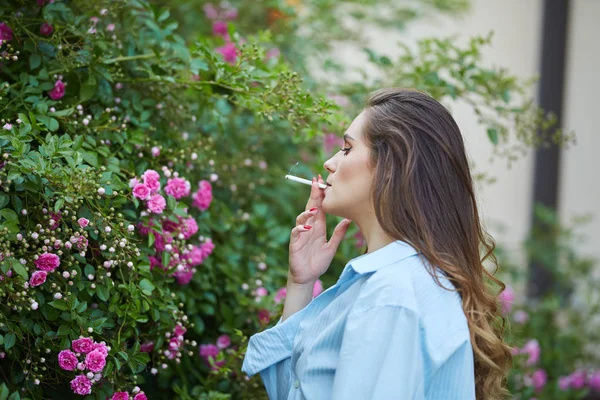 ピンクのバラの茂みが屋外カメラを見て茶色の髪の女性 — ストック写真