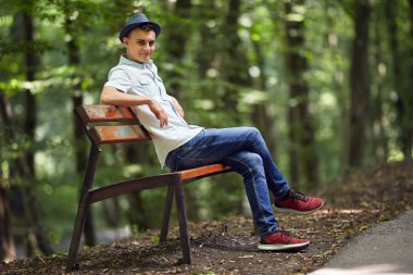 Parkta bir bankta oturan mutlu yakışıklı genç adam