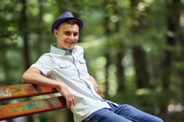 Parkta bir bankta oturan mutlu yakışıklı genç adam