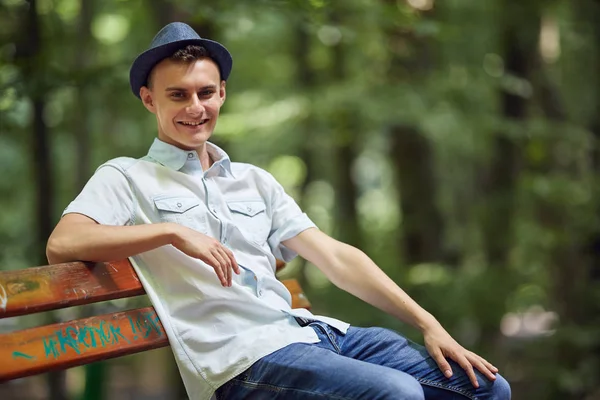 快乐英俊的年轻人坐在公园的长凳上 — 图库照片