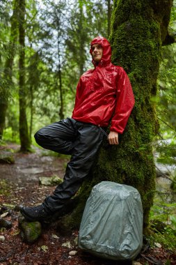 Sırt çantasında ormanda hiking yağmurluk ile genç adam