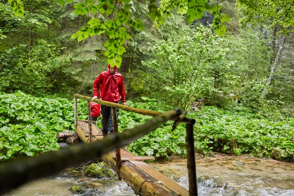 Junger Mann Regenmantel Überquert Eine Holzbrücke Über Einen Fluss — Stockfoto