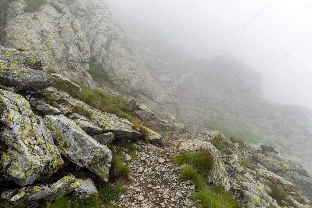 Alpine landscape with hiking trail going on the mountain in the mist