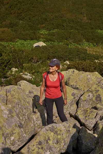 Middle aged woman with backpack hiking on trail in mountains at daytime