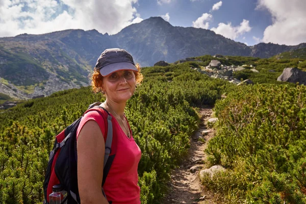 Middle aged woman with backpack hiking on trail in mountains at daytime