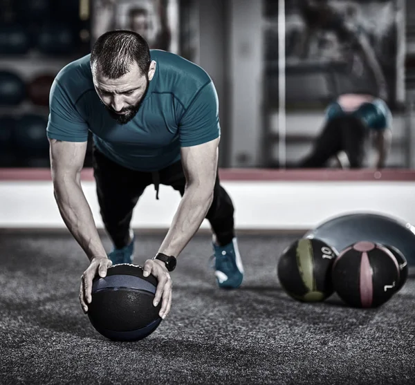 Fitness coach demonstrating push-ups on a medicine ball in the gym