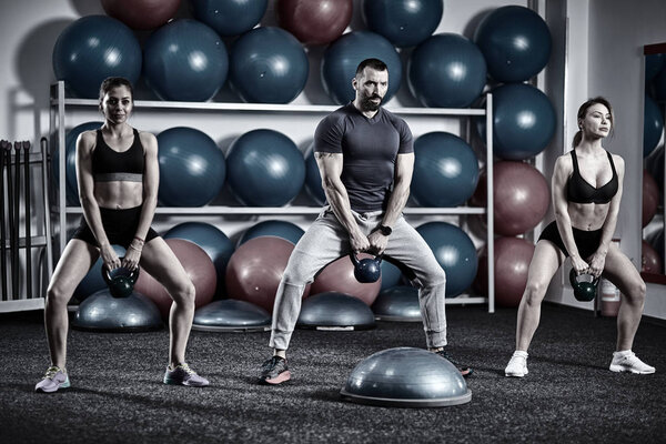 Fitness instructor with two girls working out with kettlebells