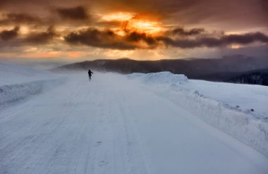 Woman walking alone in snowstorm at sunset clipart