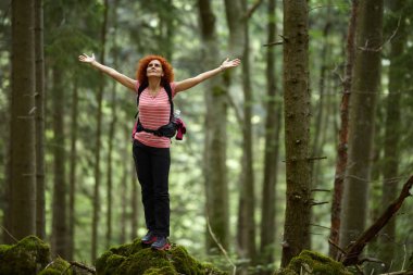 Curly redhead woman with backpack hiking on trail at daytime clipart