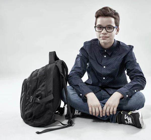 男孩与背包坐在地板上 灰色背景 — 图库照片