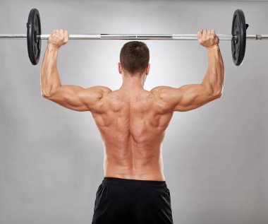 Gri arka plan üzerinde halter ile omuz egzersiz yapan erkek