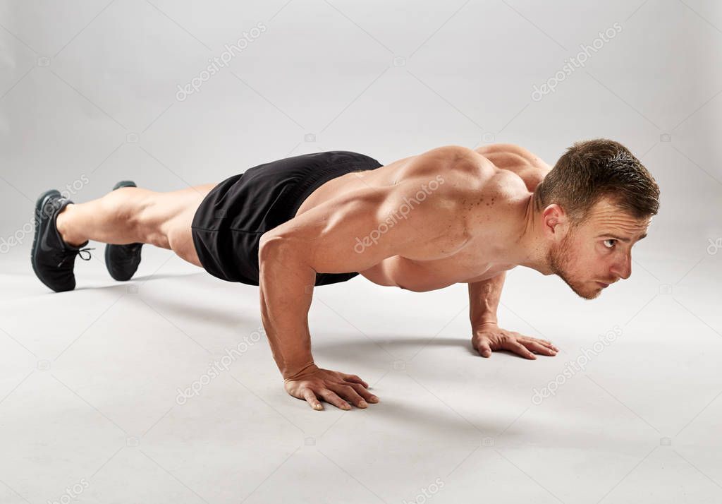 Fitness model doing pushups on gray background in studio