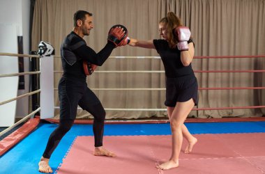 Genç bayan boksör ve koçu ringde yumruk tokuşturuyor.