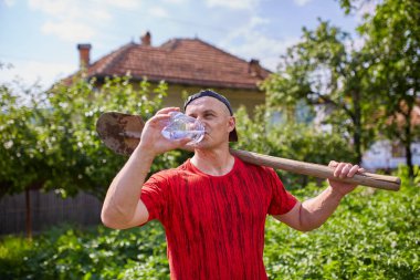 Bir çiftlikte su içen susamış işçi, elinde bir kürek