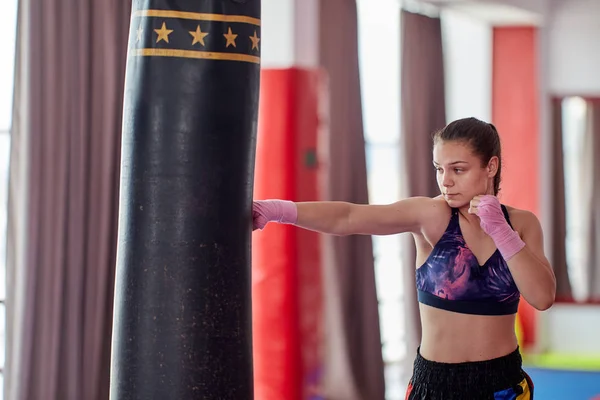 Kick-boxer female training at heavy bag with her hands wrapped