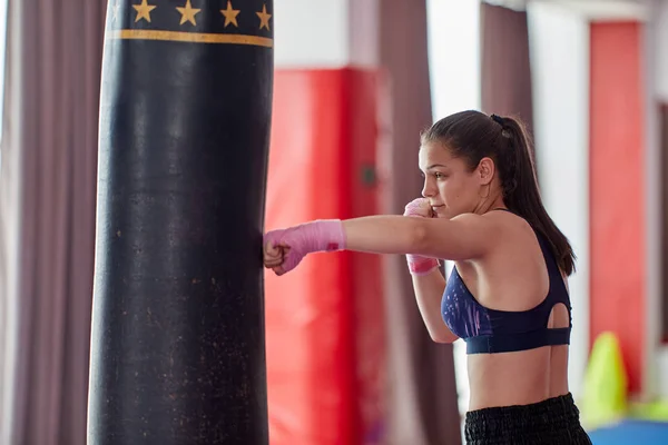 Kick-boxer female training at heavy bag with her hands wrapped