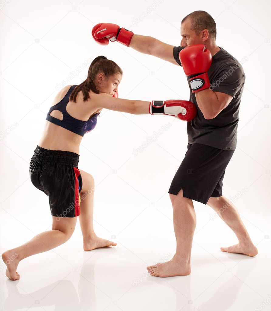 Young female kickboxer sparring with her coach on white background