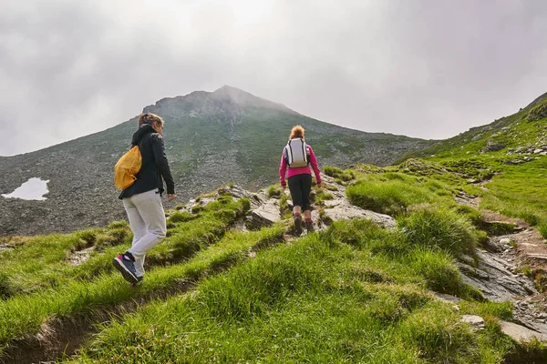 妇女背着背包在白天在岩石山脉的小径上徒步旅行 — 图库照片