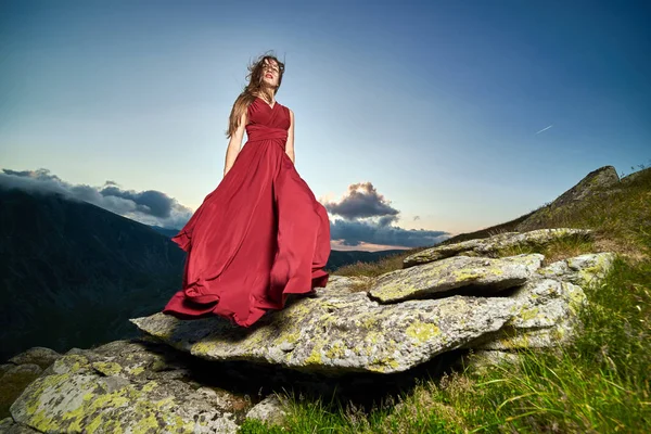 山の岩の上に赤いドレスで美しい女性のファッションモデル — ストック写真