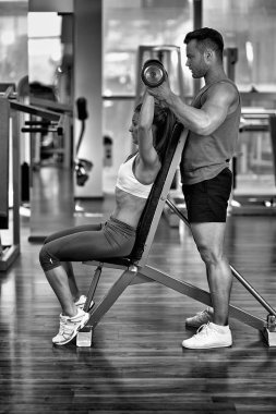 Halterlerle çalışan bir kadına kişisel antrenör yardım ediyor.