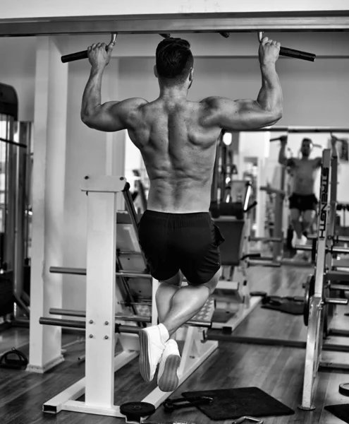 Man doing pull-ups in the gym, view from the back