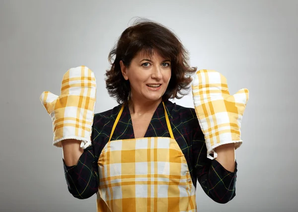 エプロンと灰色の背景の上調理手袋を持つ主婦 — ストック写真