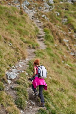 Sırt çantalı kadın, kamerayla dağ yolunda yürüyor.