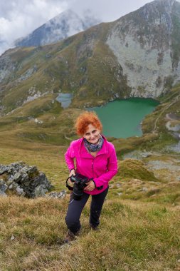 Sırt çantalı kadın, kamerayla dağ yolunda yürüyor.