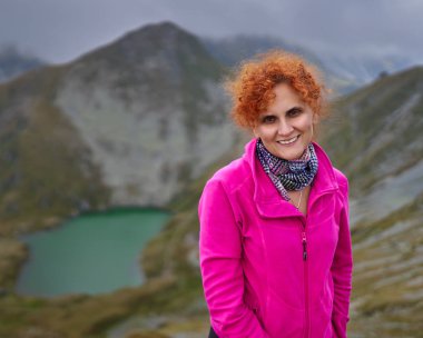 Sırt çantalı kadın, kamerayla dağ yolunda yürüyor.