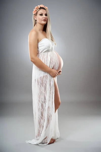 スタジオポートレートの美しいです妊娠中の女性で白い服を着て横にグレースタジオの背景 — ストック写真