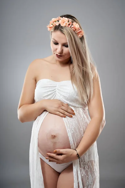スタジオポートレートの美しいです妊娠中の女性で白い服を着て横にグレースタジオの背景 — ストック写真