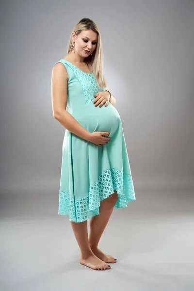 一个穿着青色衣服站在灰色背景上的孕妇的工作室肖像 — 图库照片
