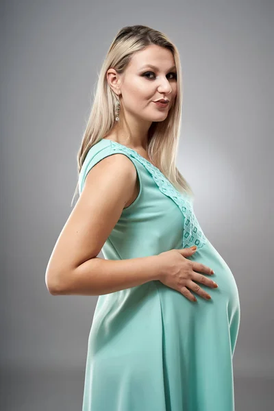 スタジオポートレートの妊娠中の若いです女性でシアンドレス上の灰色の背景 — ストック写真