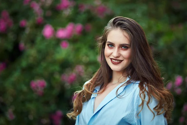 Closeup of a young woman by a rose bush in the garden