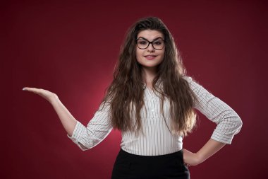 Çekici bir iş kadını, kırmızı arka planda görünmez bir ürün sunuyor.