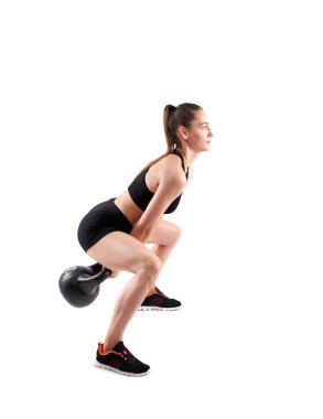 Genç atletik kadın beyaz arka planda yalnız başına kettlebell ile egzersiz yapıyor.