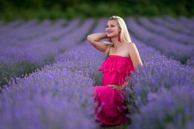 Lavanta tarlasında çeşitli pozlarda pembe elbiseli genç sarışın kadın.