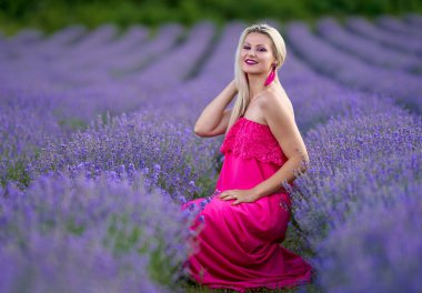 Lavanta tarlasında çeşitli pozlarda pembe elbiseli genç sarışın kadın.