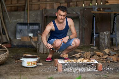 Genç adam barbeküde çeşit çeşit et pişiriyor.