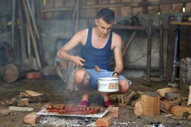 Genç adam barbeküde çeşit çeşit et pişiriyor.