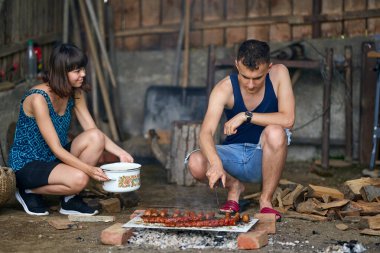 Mutlu genç çift kırsalda barbekü yapıyor.