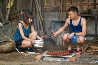 Mutlu genç çift kırsalda barbekü yapıyor.