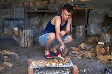 Genç adam barbeküde çeşit çeşit et pişiriyor.