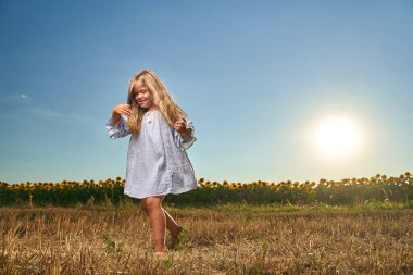 Ayçiçeği tarlasının önünde dans eden mutlu küçük kız