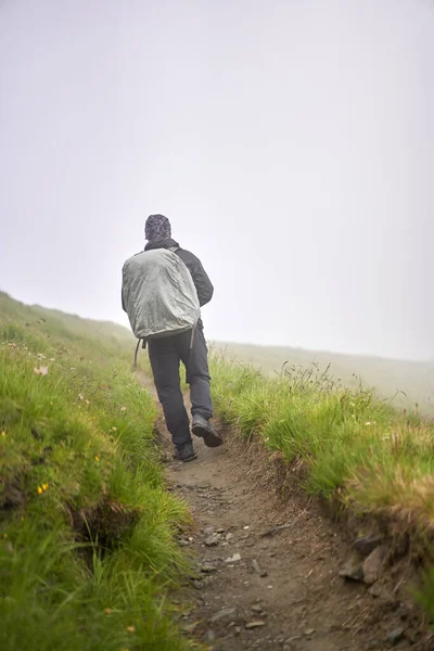 带着雨衣和大背包的远足者徒步旅行到高地 — 图库照片