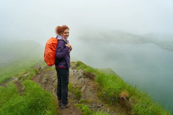 背着背包在雾气中冰湖边小径上徒步旅行的女人 免版税图库照片