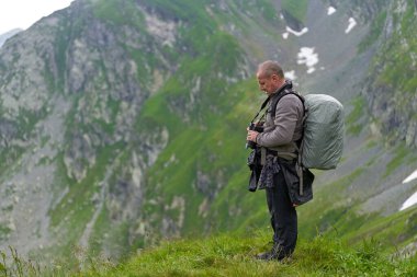 Kameralı ve büyük sırt çantalı profesyonel doğa fotoğrafçısı dağlara doğru yürüyor.