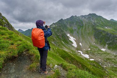 Kameralı ve sırt çantalı profesyonel fotoğrafçı dağlara doğru yürüyor.