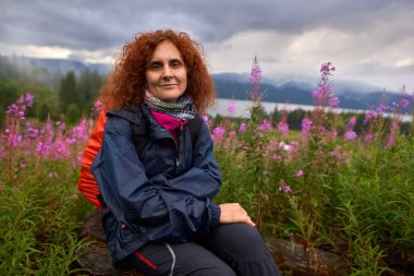 Yürüyüşten sonra sırt çantalı bir kadın çiçek tarlasında dinleniyor.