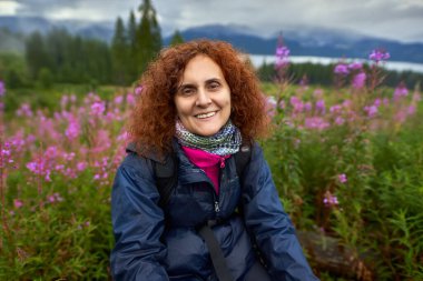 Yağmurlu bir günde sırt çantalı bir kadın dağ çiçekleri tarlasında yürüyüş yapıyor.